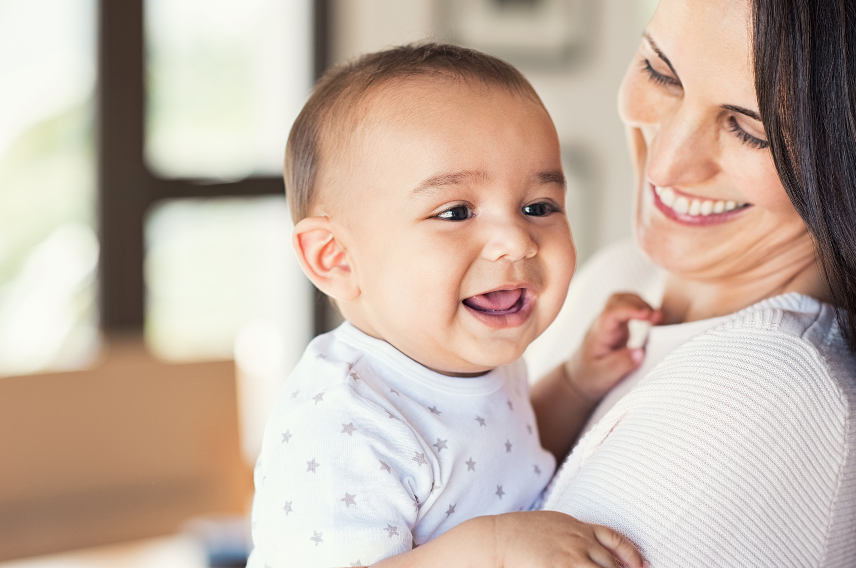 Portrait of a cute newborn baby in mother's hands. Beautiful mom holding cute son laughing. Closeup of mid woman with her little boy. New family and love concept.